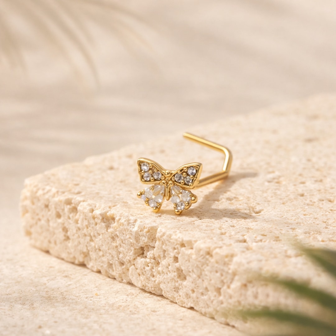 Stud de nez papillon doré serti de zircons blancs, tige coudée en L, posé sur une pierre beige