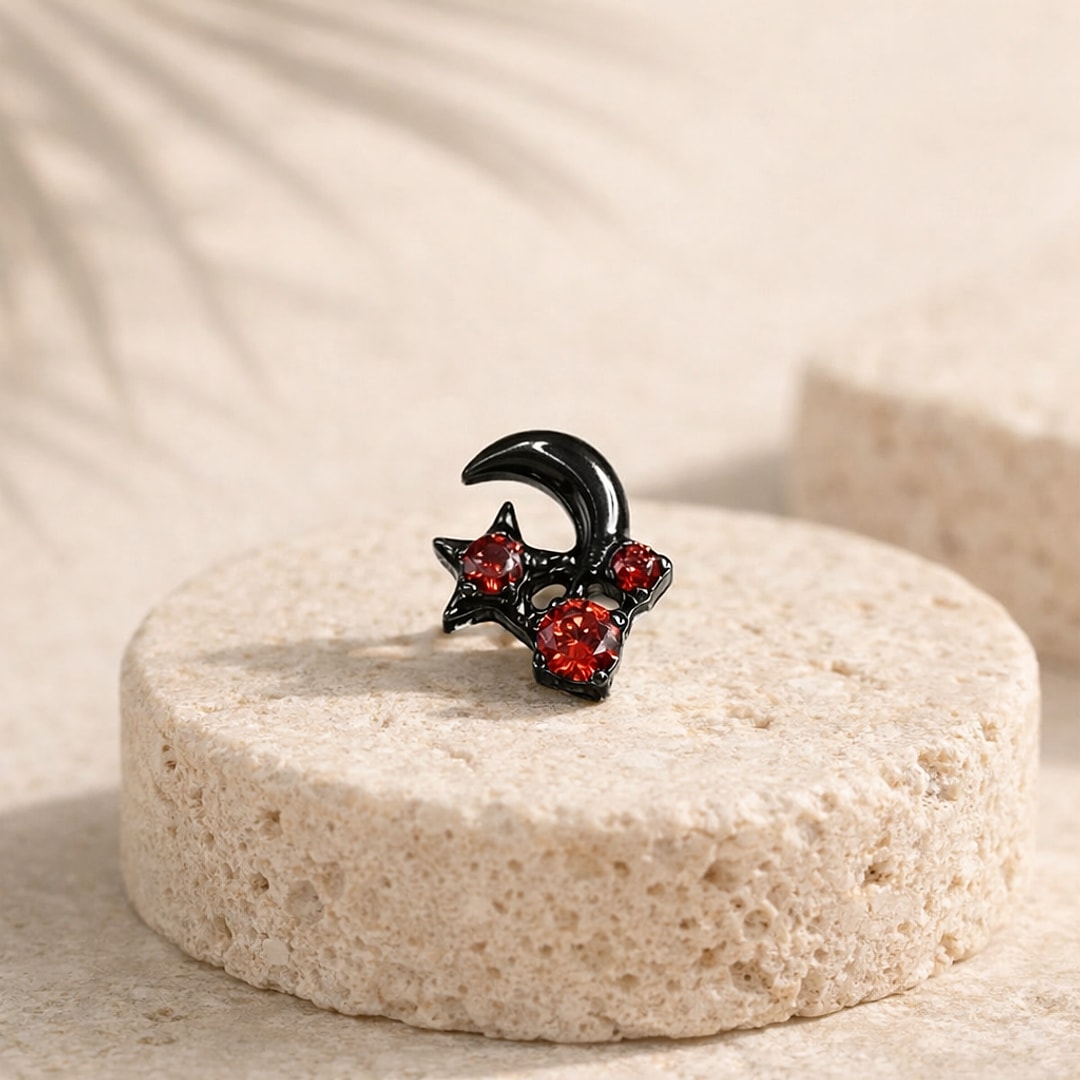 Stud flat back en titane noir en forme de croissant de lune et étoile serti de trois zircons rouges, posé sur une pierre claire