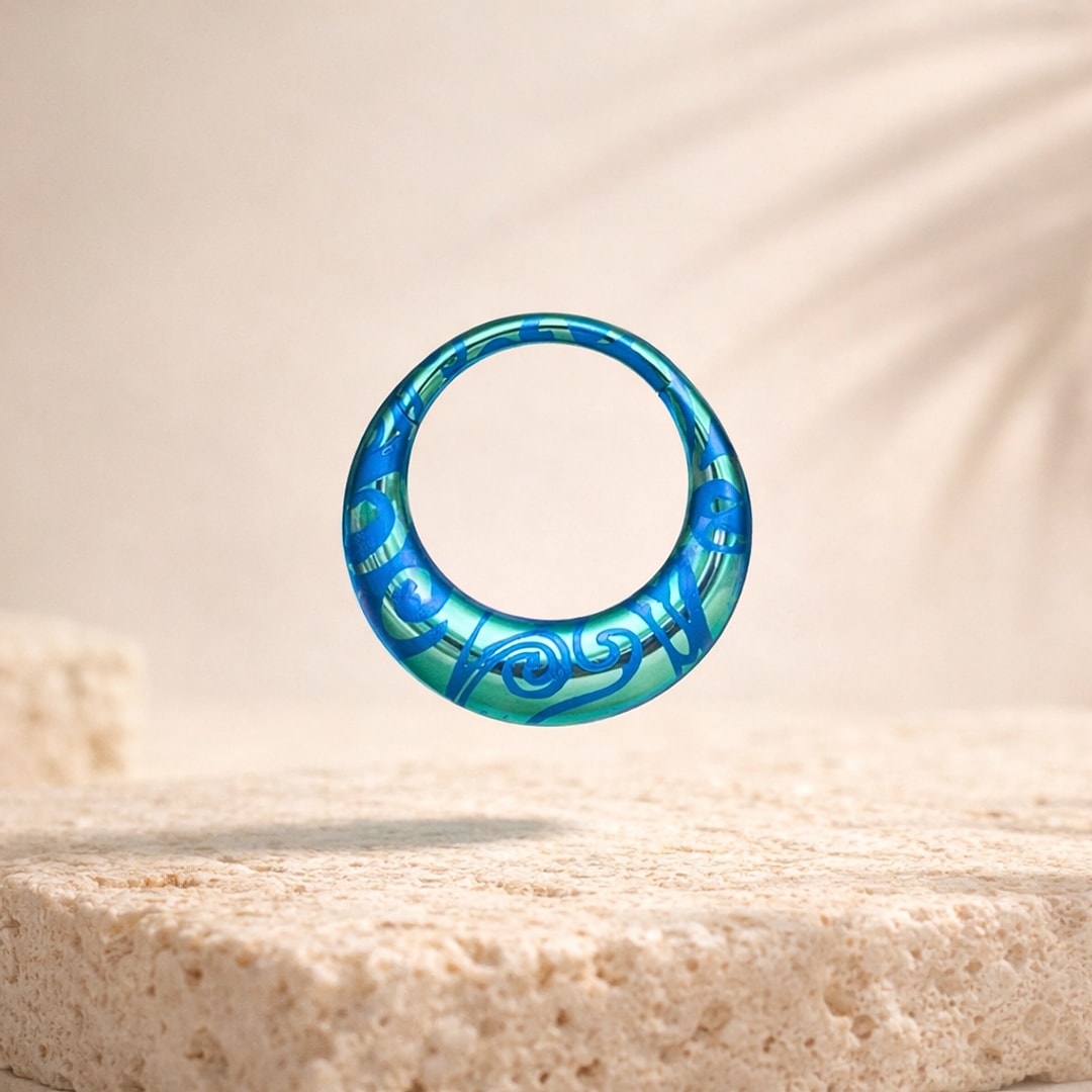Anneau de piercing en titane anodisé bleu vert orné de volutes gravées, posé sur une pierre claire