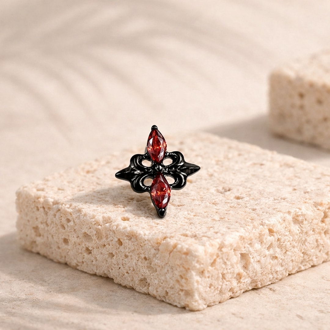 Stud flat back en titane noir en forme de croix baroque, serti de deux zircons rouges marquise, posé sur une pierre claire