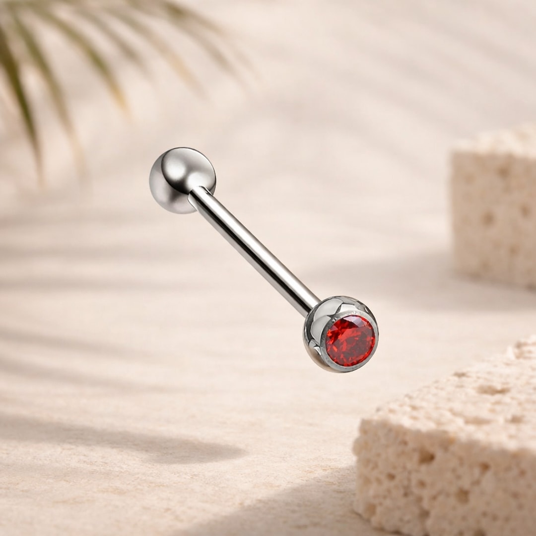 Barre de langue en titane avec bille lisse et zircon rouge rond serti, posée sur fond beige
