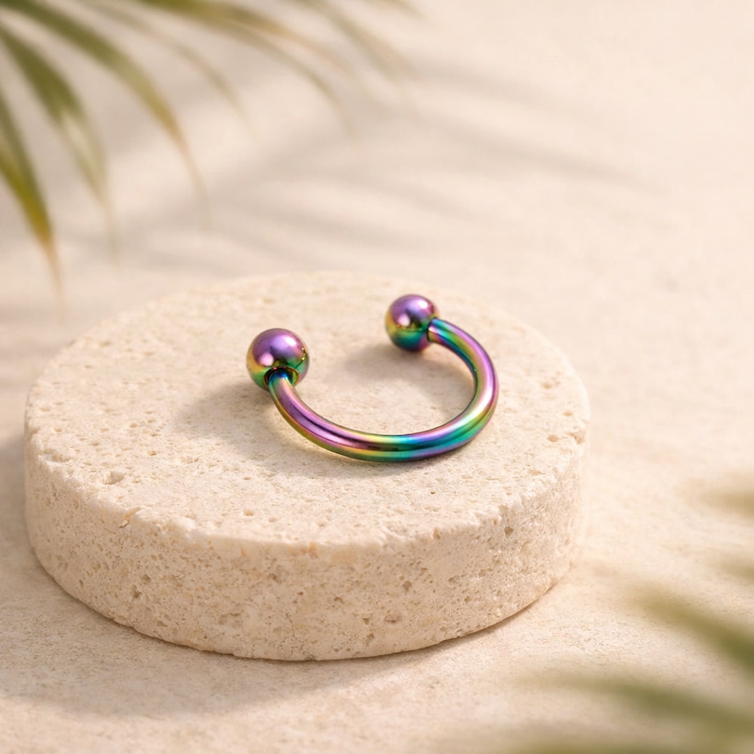 Fer à cheval en titane multicolore arc-en-ciel avec deux billes, posé sur un socle de pierre claire
