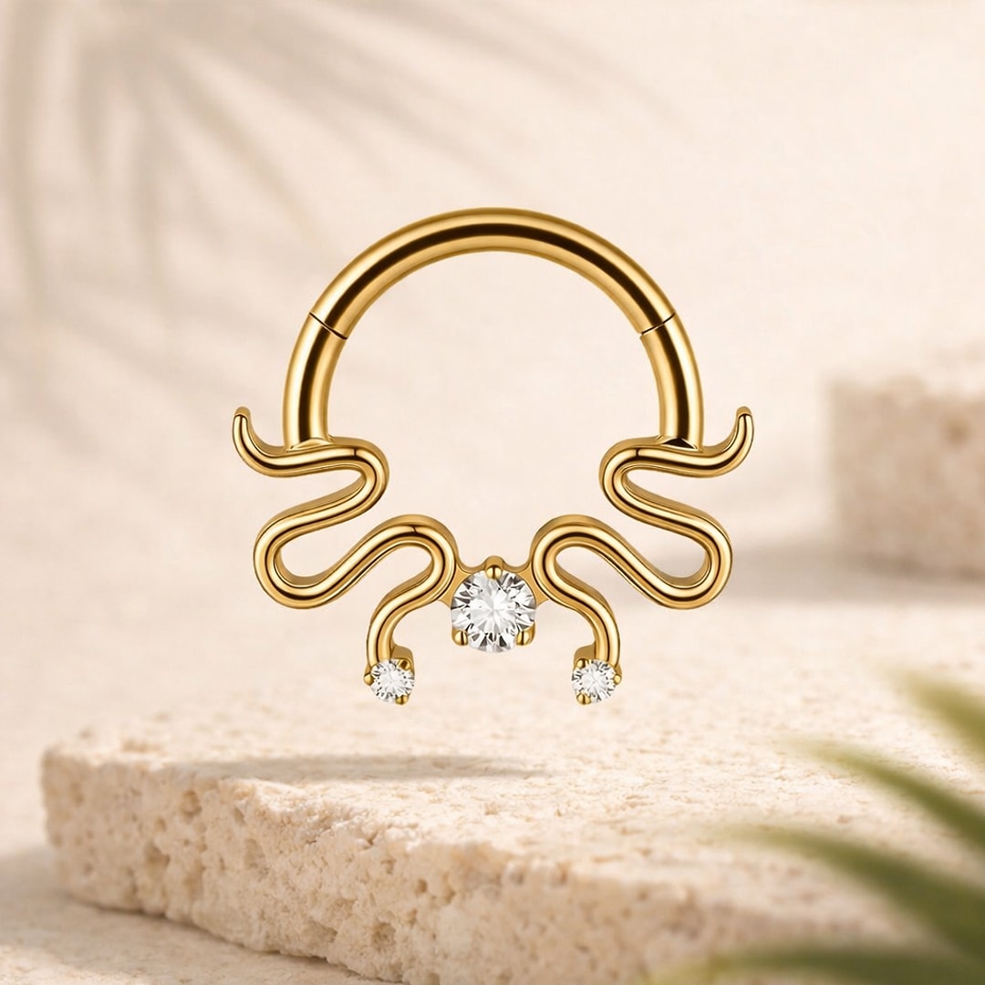 Clicker de septum en titane doré, arabesques ondulées et trois zircons blancs, posé sur une pierre claire