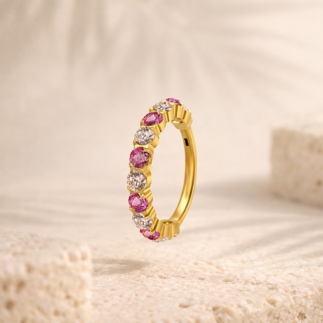 Anneau clicker en titane doré serti de zircons roses et blancs alternés, posé sur une pierre claire