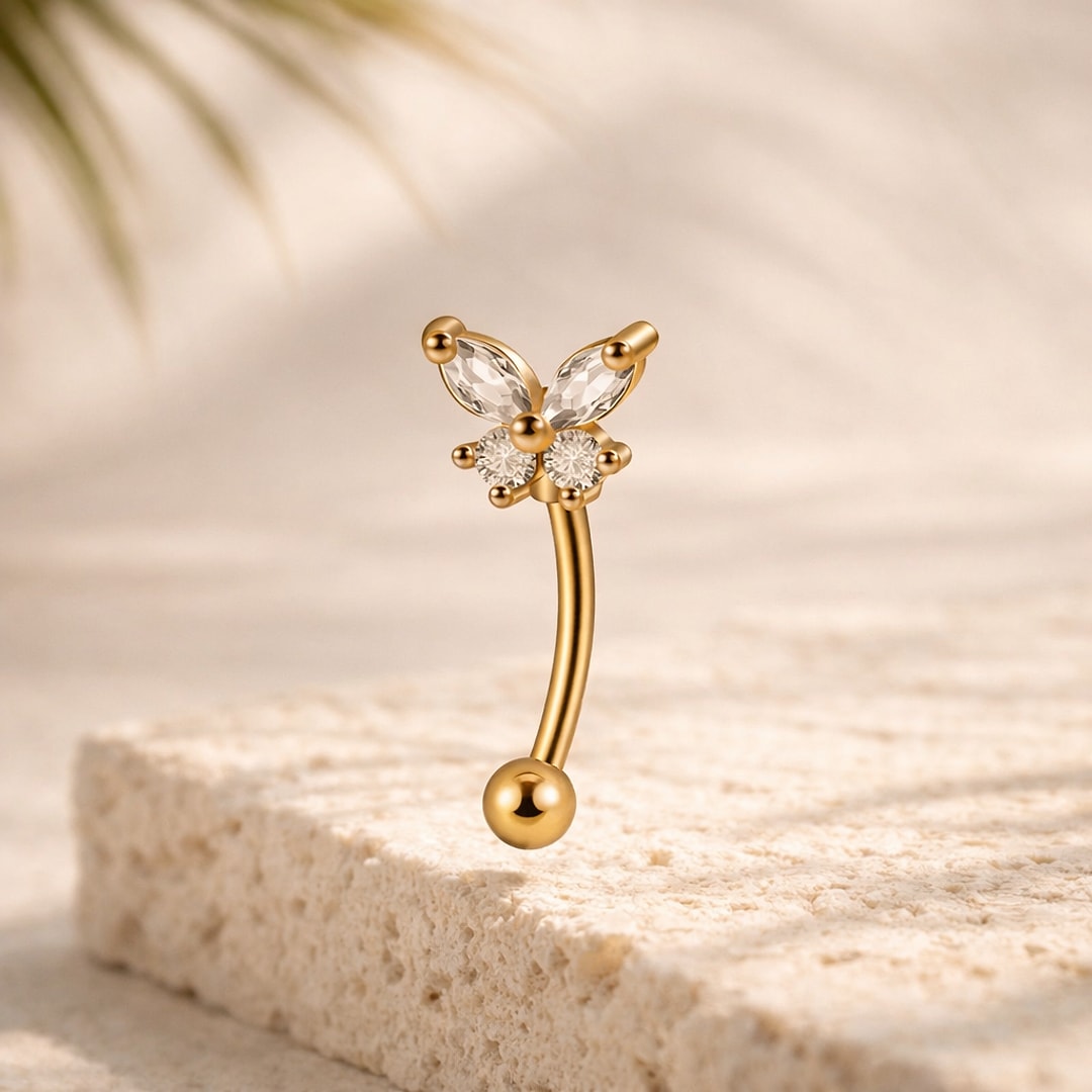 Banane de nombril en titane doré, motif papillon serti de zircons blancs, posée sur une pierre claire
