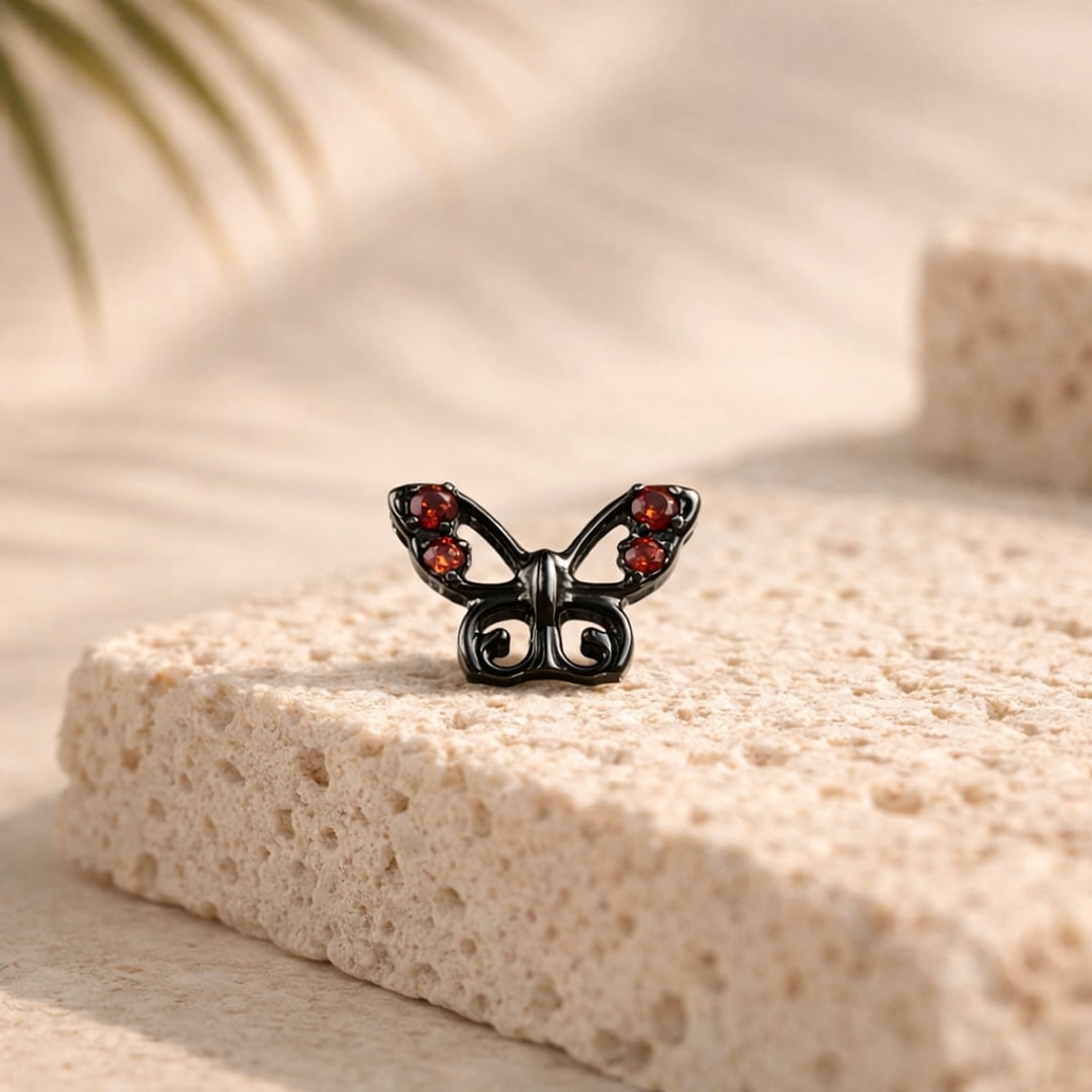 Stud flat back papillon en titane noir serti de quatre zircons rouges, posé sur une pierre claire
