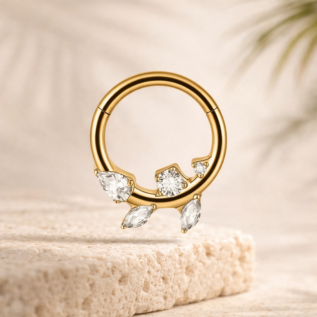 Anneau clicker septum en titane doré orné de zircons blancs marquise et goutte, posé sur une pierre claire