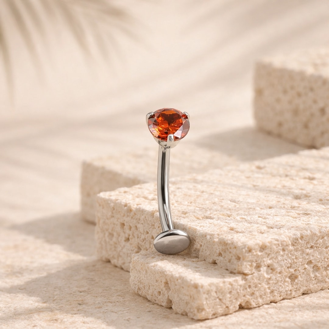 Banane de piercing nombril en titane argenté avec zircon rouge rond serti quatre griffes, posée sur pierre claire