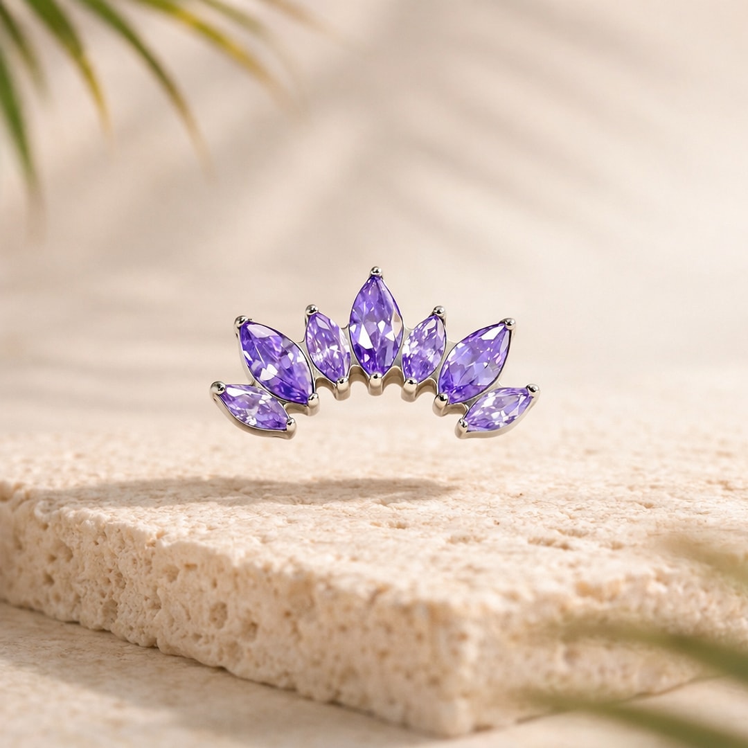 Top de piercing en titane argenté formant une couronne de sept zircons violets taille navette, posé sur une pierre claire