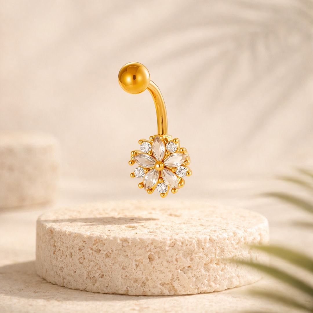 Banane de nombril en acier doré avec fleur sertie de cristaux blancs taille marquise, posée sur une pierre claire