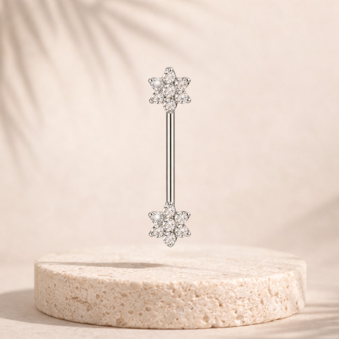 Barbell de téton en titane argenté avec deux fleurs de zircons blancs posé sur un socle en pierre claire