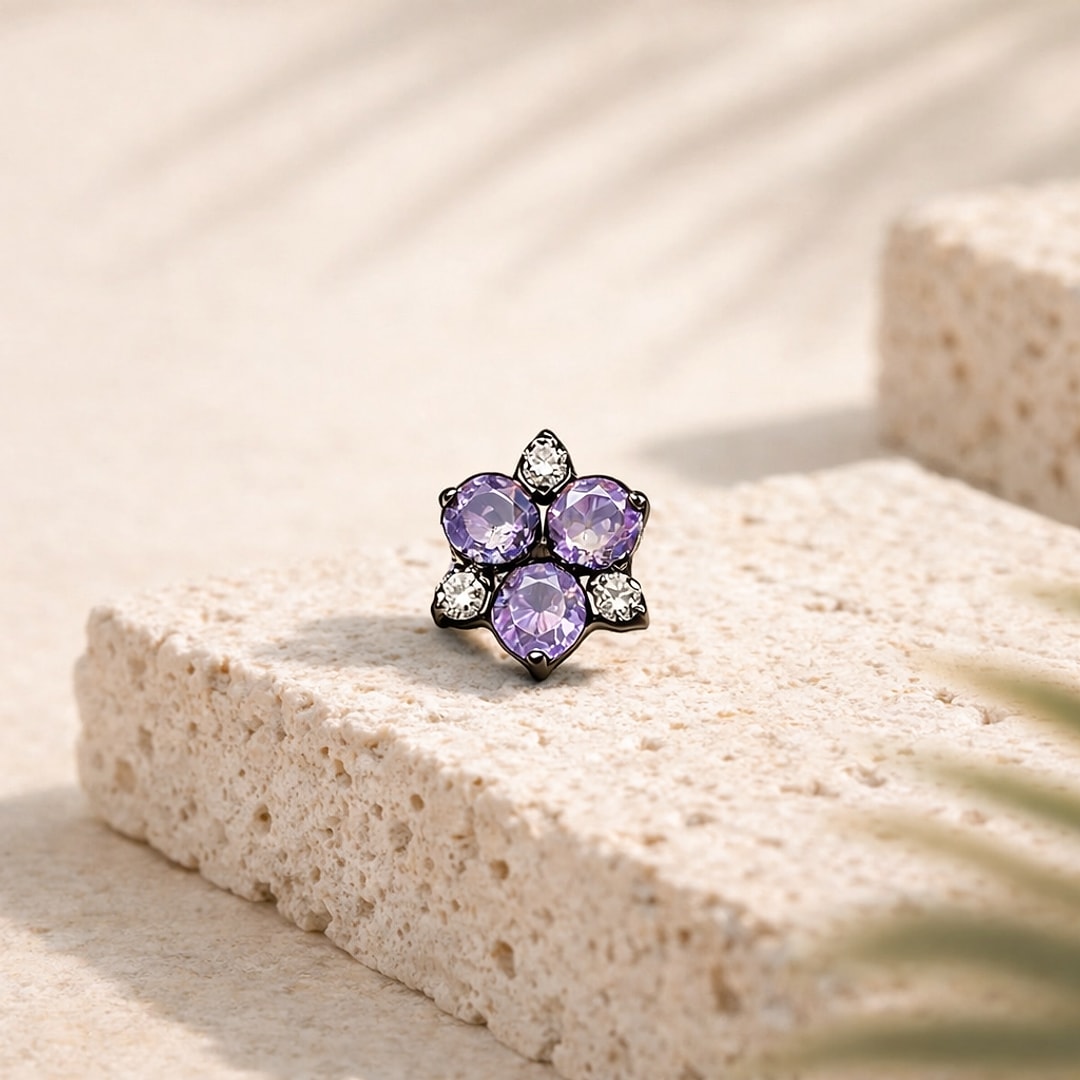 Stud flat back en titane noir en forme de fleur, zircons violets et blancs, posé sur une pierre claire