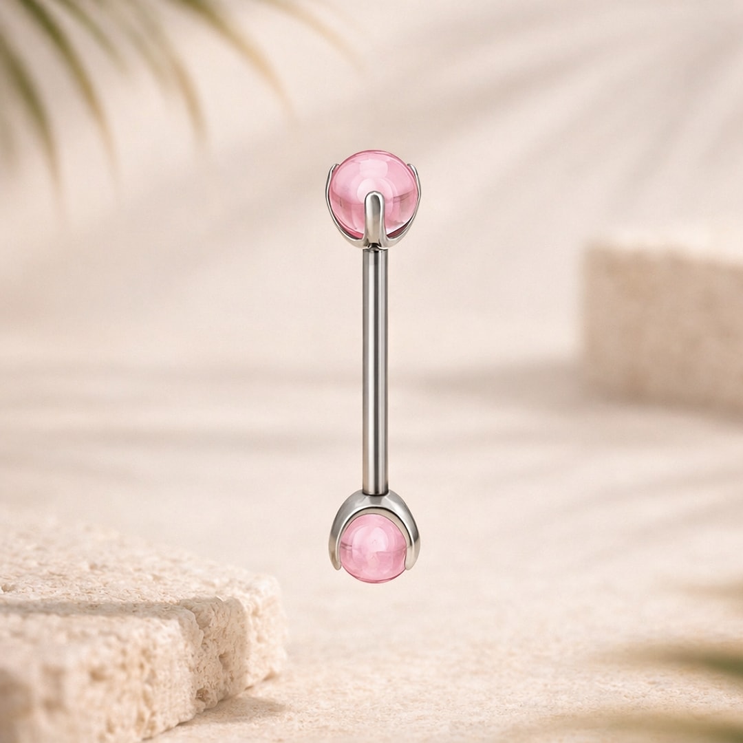 Barre de langue en titane argenté avec deux cabochons ronds roses sertis griffes, sur fond beige