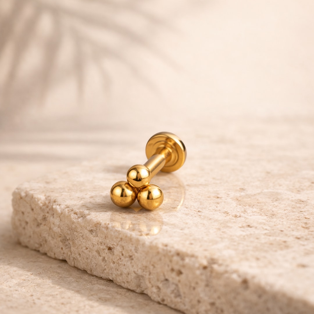 Labret doré à trois billes polies posé sur une pierre beige