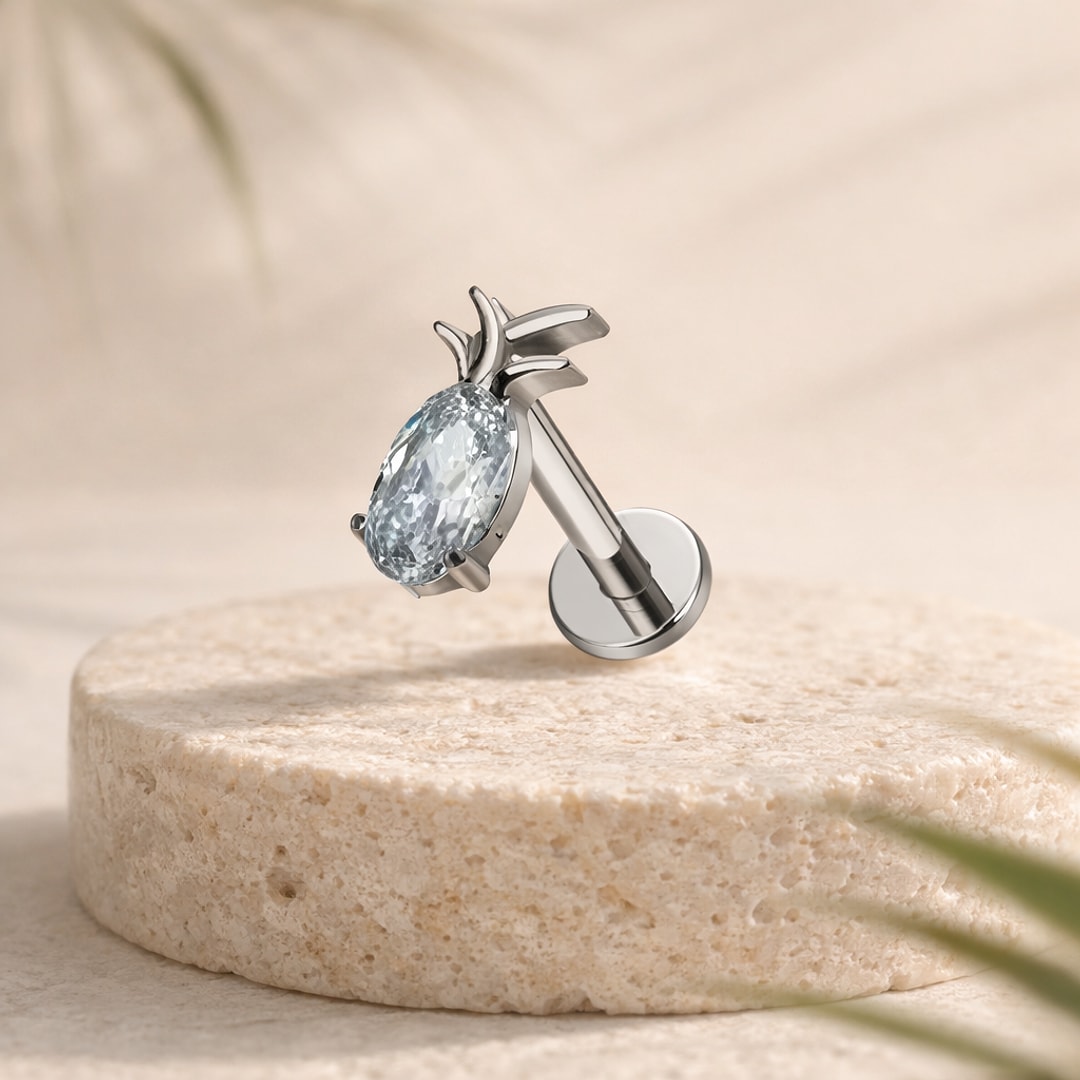 Stud flat back ananas en titane argenté avec zircon ovale facetté et feuilles polies, posé sur une pierre claire