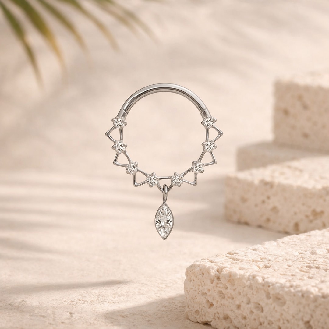Bijou de piercing en titane argenté, couronne de zircons sertis et pendentif navette, posé sur pierre claire