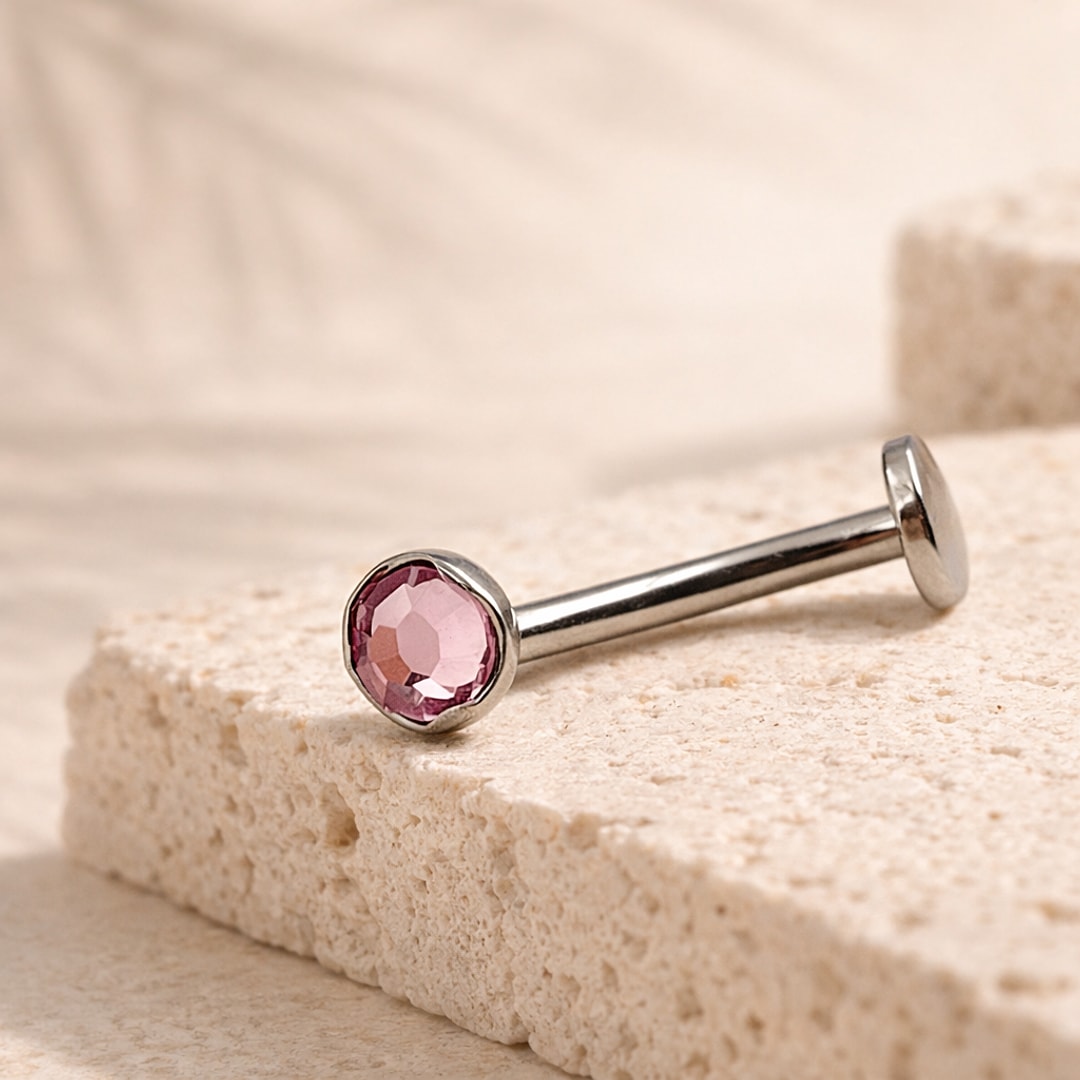 Bijou de nombril en titane argenté avec cristal rose rond serti et disque plat, posé sur pierre claire