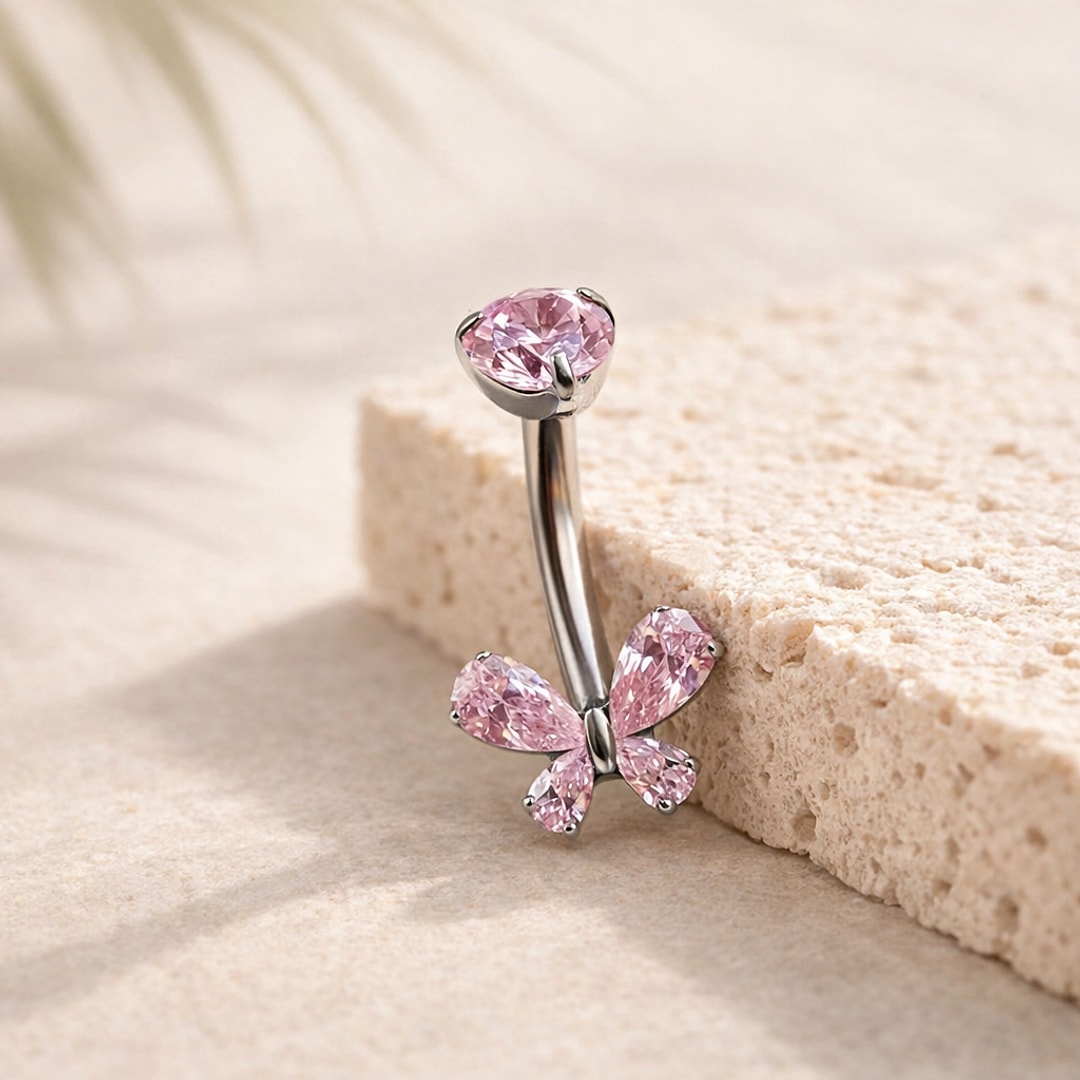 Banane de nombril en titane argenté avec papillon et pierre ronde en zircons roses, posée sur une pierre claire