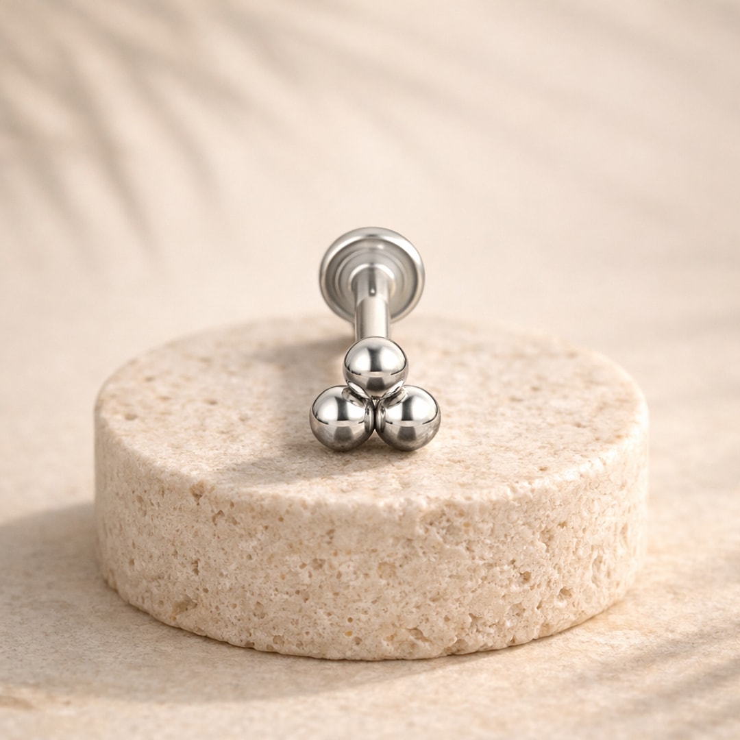 Labret en acier chirurgical argenté orné de trois billes rondes, posé sur un socle de pierre claire