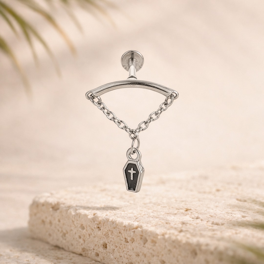 Labret acier argenté avec chaînette et pendentif cercueil noir gravé d'une croix, posé sur une pierre claire