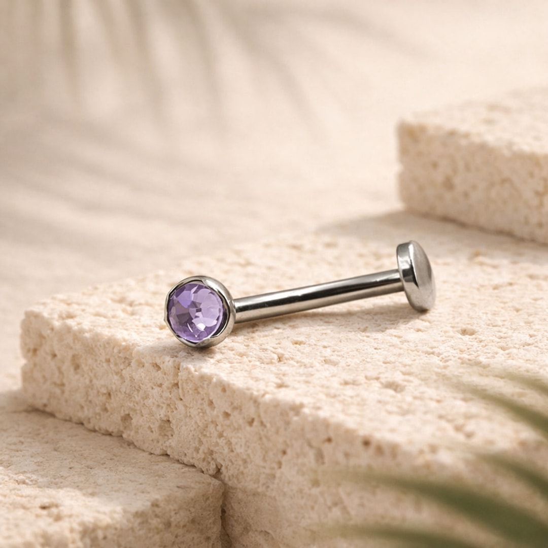 Bijou de nombril en titane argenté avec cristal violet serti et disque plat, posé sur une pierre claire