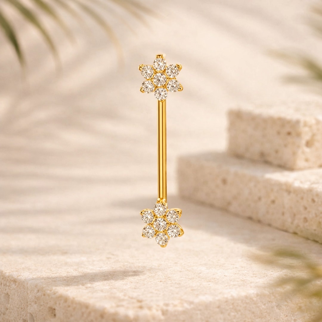 Barbell de téton en titane doré avec deux fleurs de zircons blancs posé sur une pierre claire
