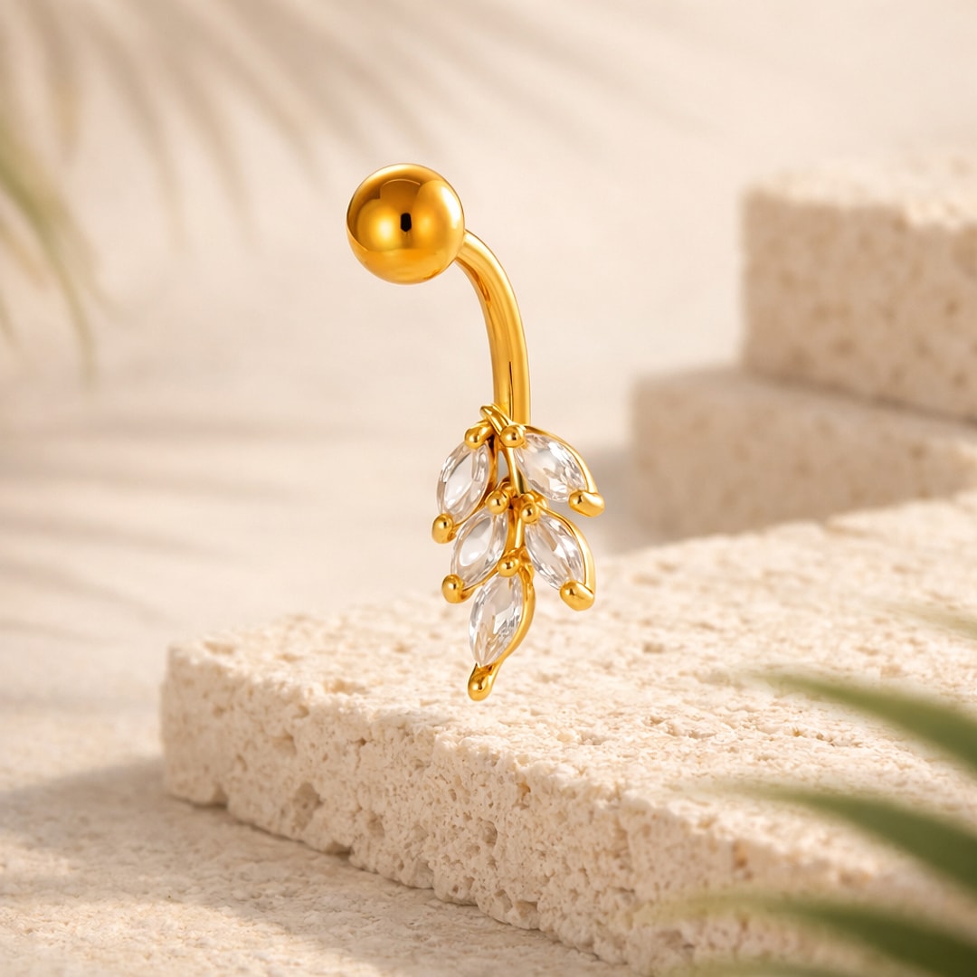 Banane de nombril dorée avec pendentif feuilles serties de cristaux transparents, posée sur pierre claire