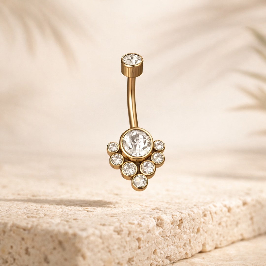 Banane de nombril dorée avec grand cristal rond entouré de sept petites pierres, posée sur une pierre claire