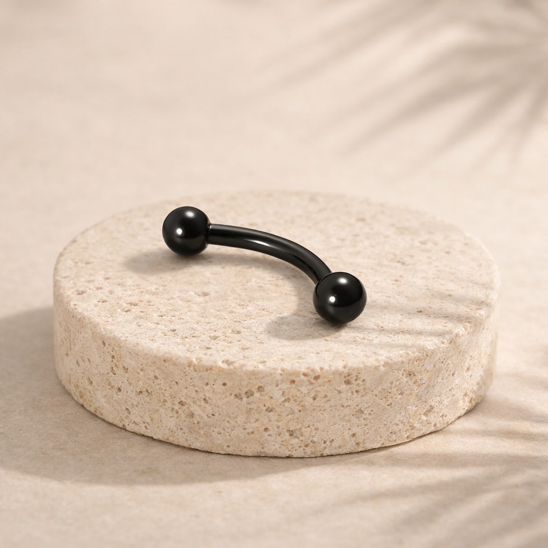 Barbell courbé noir en titane avec deux billes, posé sur un socle de pierre beige