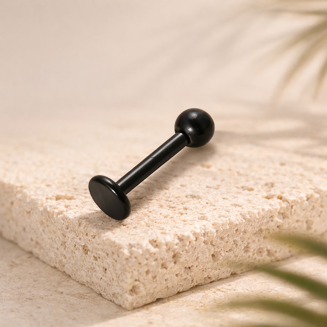Labret droit noir en titane avec boule et base plate, posé sur une pierre beige