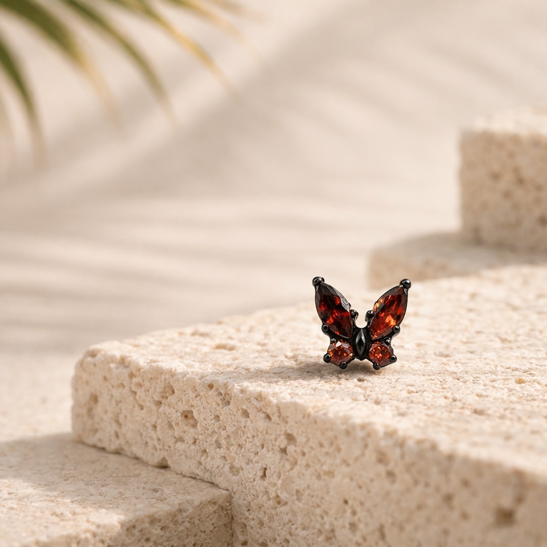 Stud flat back papillon en titane noir serti de zircons rouges, posé sur une pierre claire