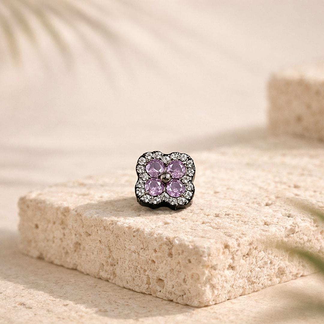 Stud de nez en titane noir, fleur à quatre zircons violets cerclée de petits strass, posé sur une pierre claire