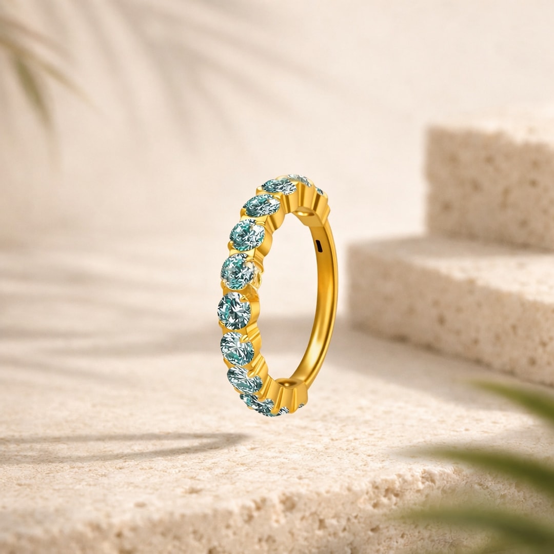 Clicker en titane doré serti d'une ligne de zircons ronds turquoise, posé sur une pierre claire