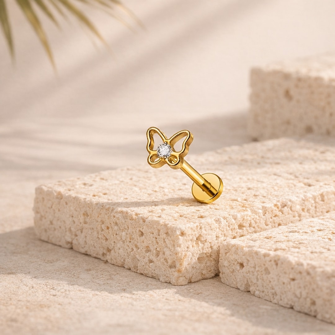 Stud flat back titane doré avec papillon ajouré et zircon blanc, posé sur une pierre claire