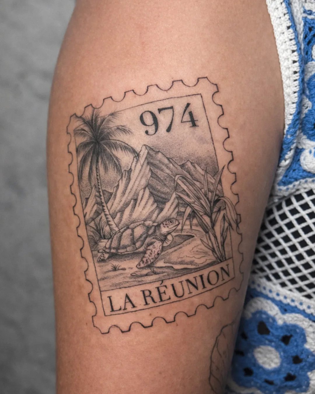 Tatouage 974 en forme de timbre « La Réunion » avec palmiers, montagnes et tortue, réalisé par David à Saint-Louis