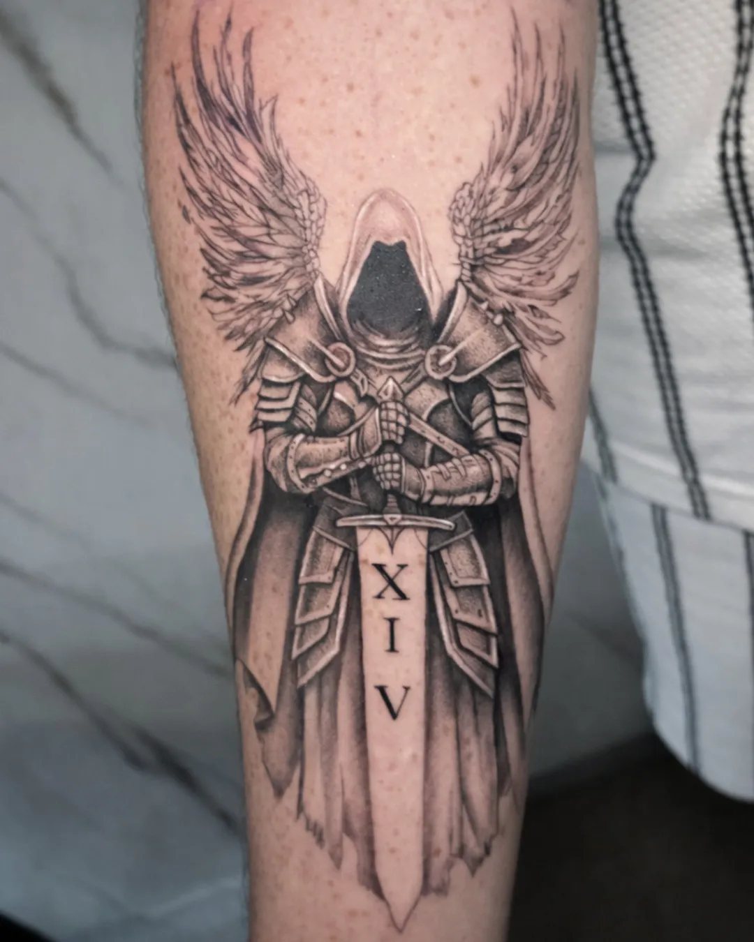 Tatouage ange guerrier avec épée et chiffres romains sur l’avant-bras