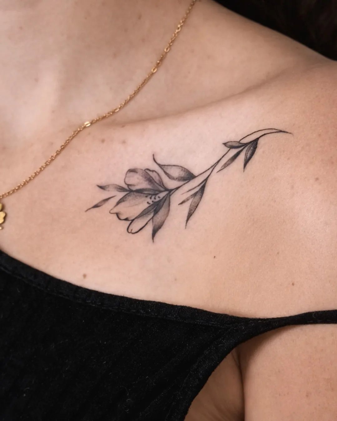 Tatouage branche fleurie en fine line sur la clavicule
