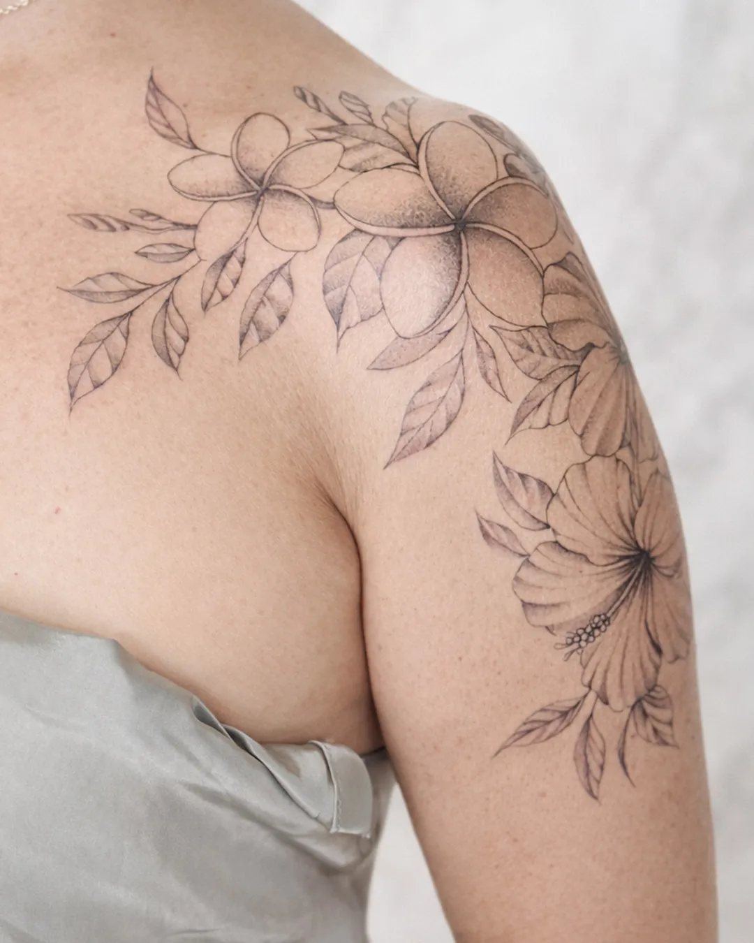 Tatouage femme en fine line, fleurs de frangipanier et d’hibiscus sur l’épaule, réalisé par Mathieu à Saint-Louis, La Réunion