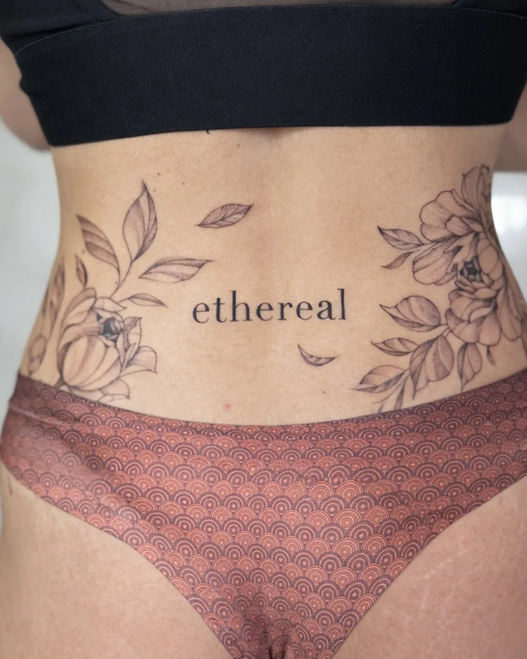 Tatouage femme fleurs et mot « ethereal » sur le bas du ventre