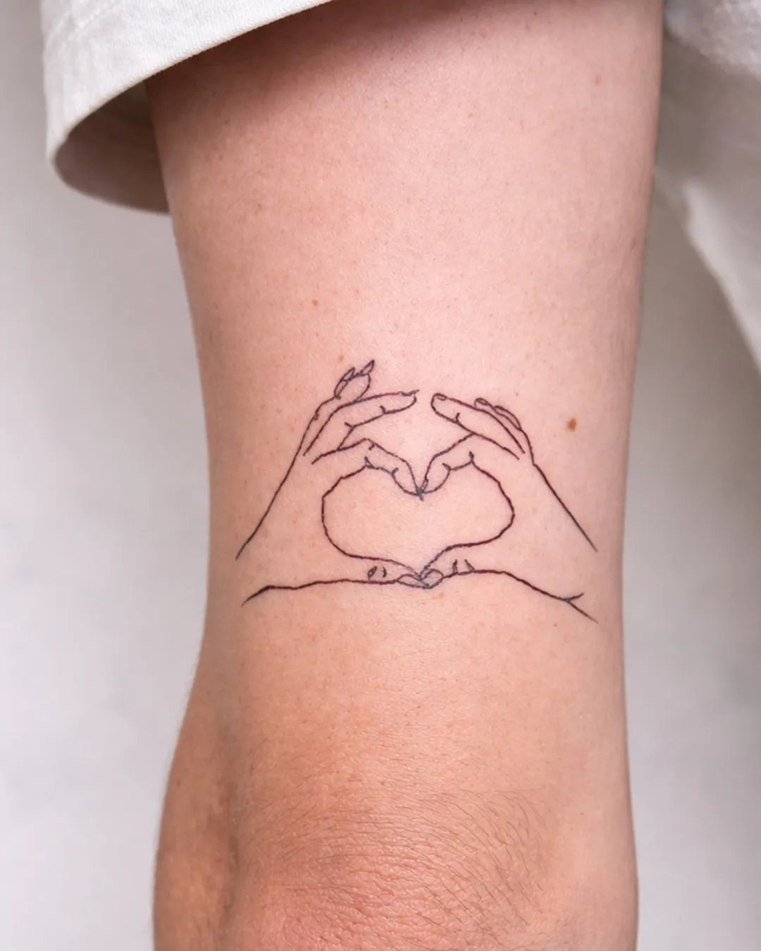 Tatouage fine line de deux mains formant un cœur