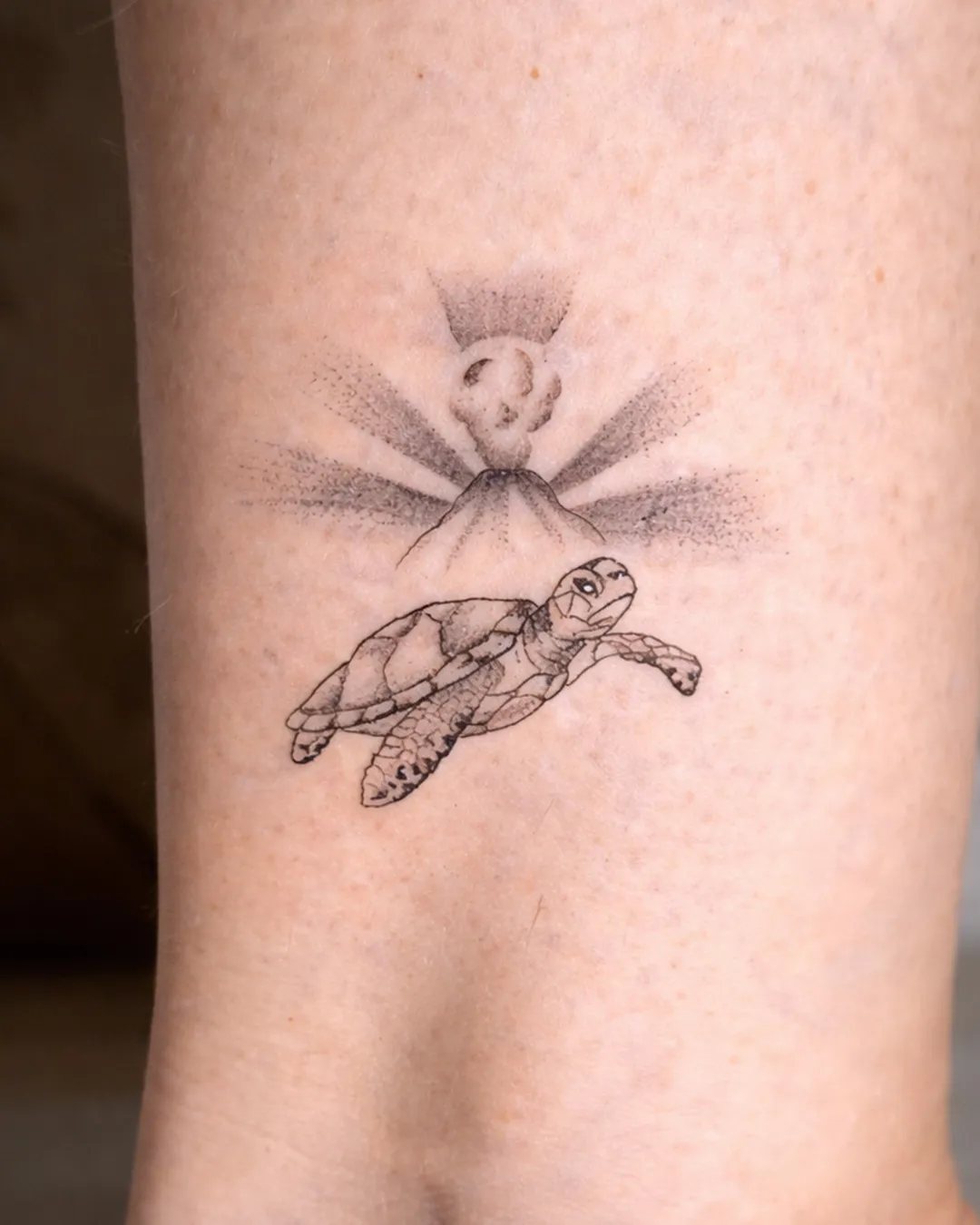 Tatouage fine line d’une tortue marine devant le volcan