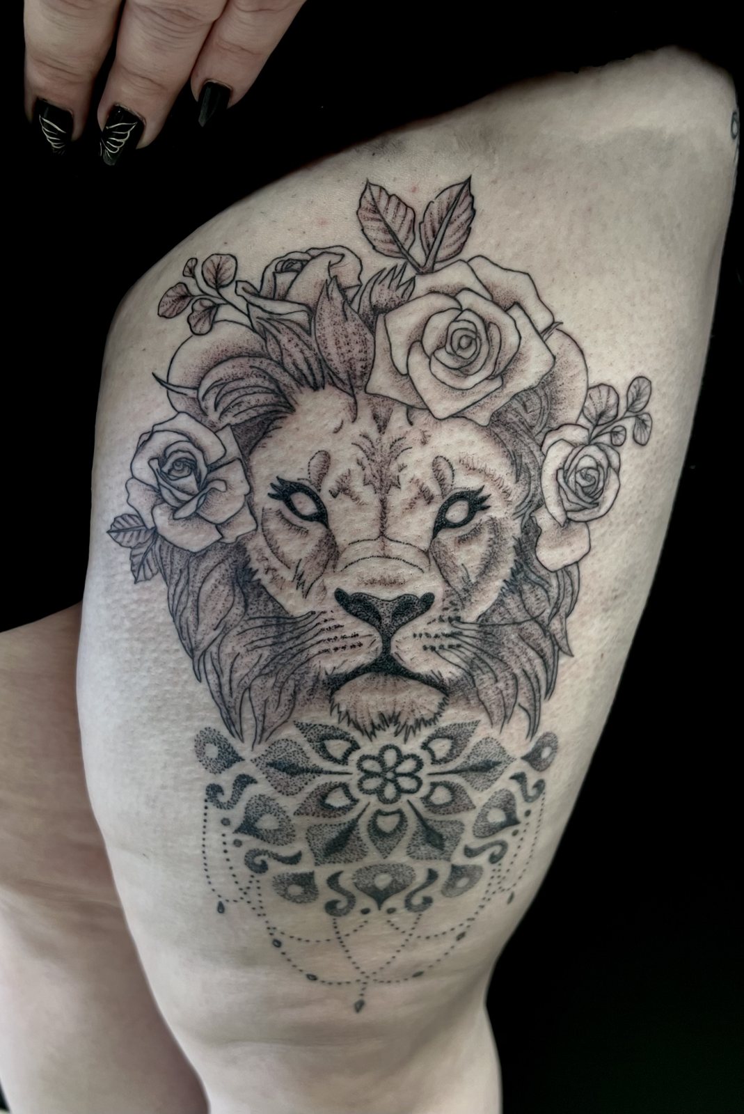 Tatouage lion entouré de roses et de motifs ornementaux sur la cuisse