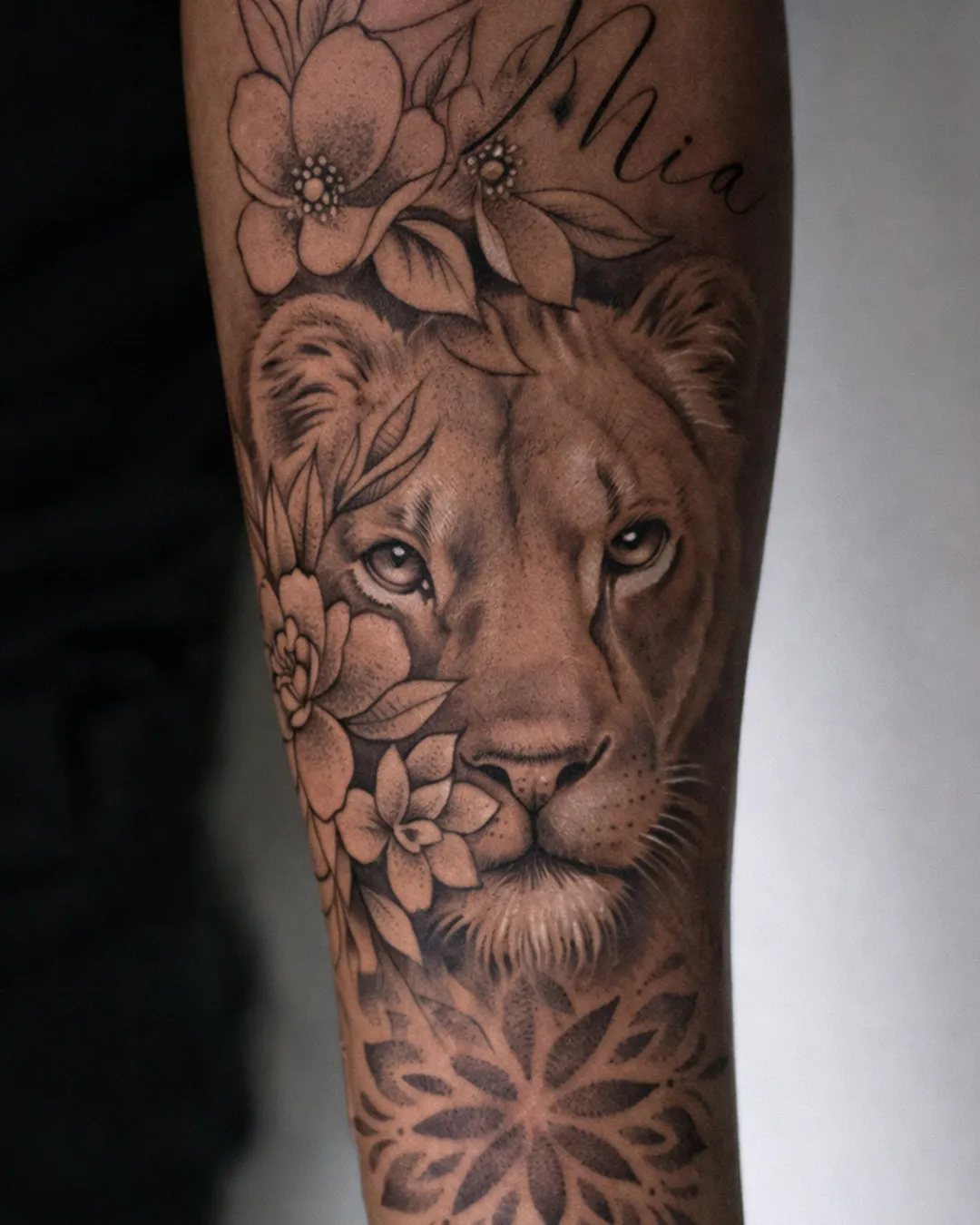 Tatouage lion réaliste en black and grey avec des fleurs sur l’avant-bras, réalisé par Jordan à Saint-Denis, La Réunion