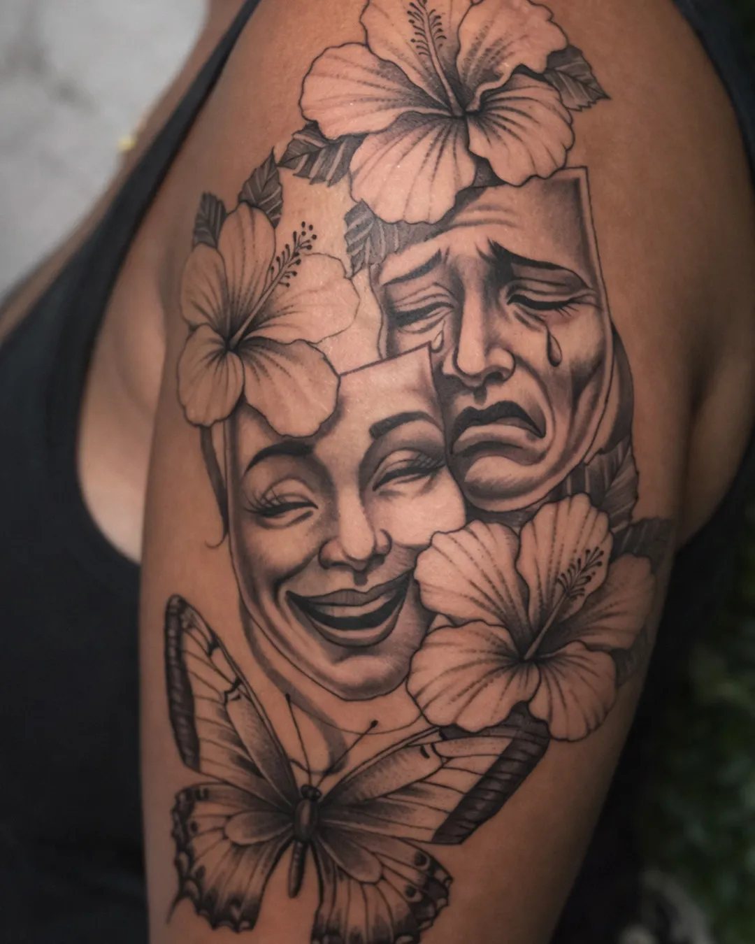 Tatouage masques de théâtre, hibiscus et papillon sur l’épaule