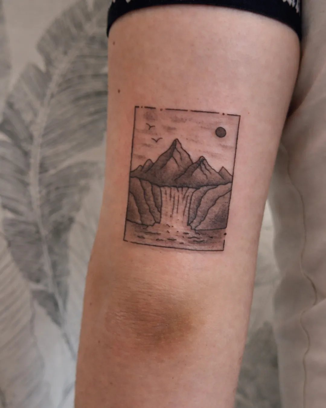 Tatouage paysage de montagnes et cascade encadré sur l’arrière du bras