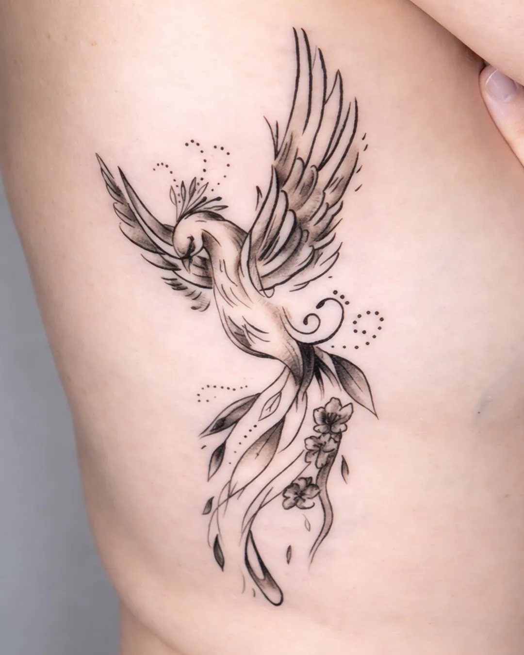 Tatouage phénix en fine line avec des fleurs sur les côtes