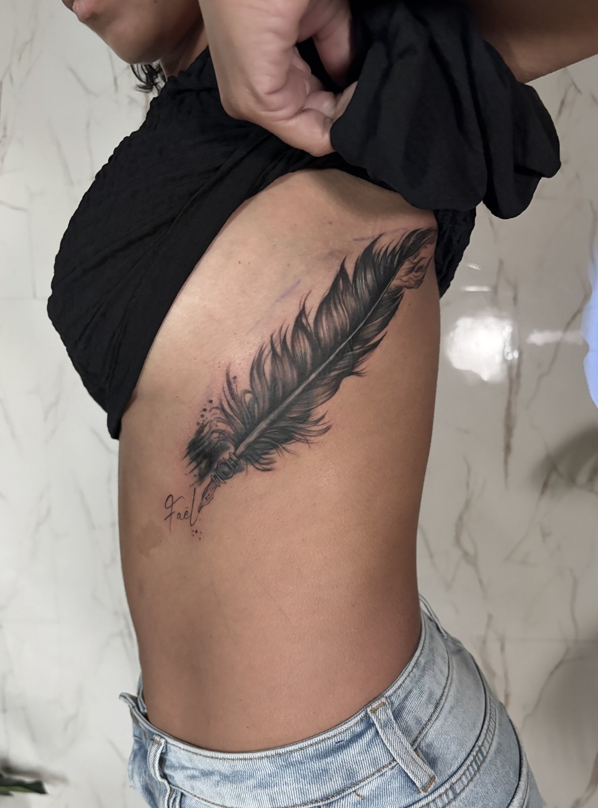 Tatouage plume réalisé en recouvrement sur les côtes