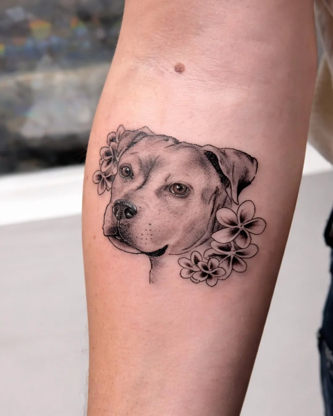 Tatouage réaliste d’un chien avec des fleurs sur le bras
