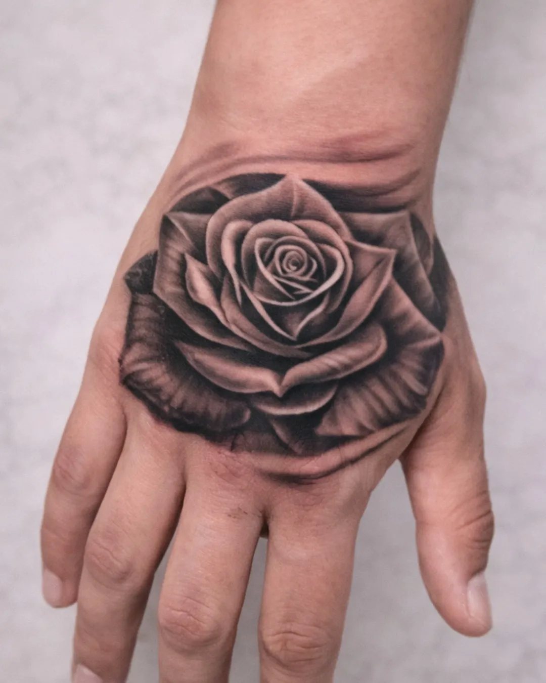 Tatouage rose réaliste en black and grey sur la main