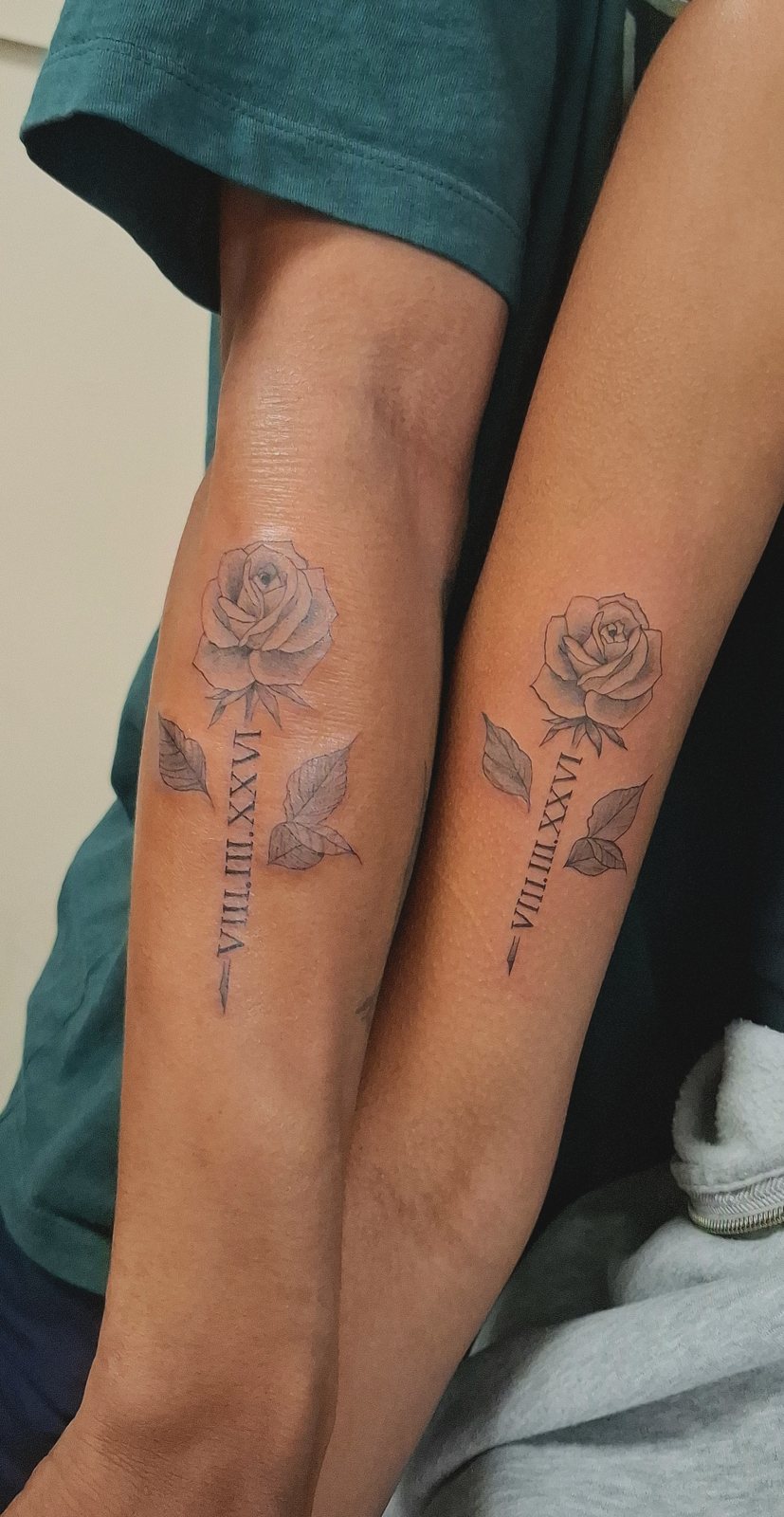 Tatouages assortis rose et chiffres romains sur deux avant-bras